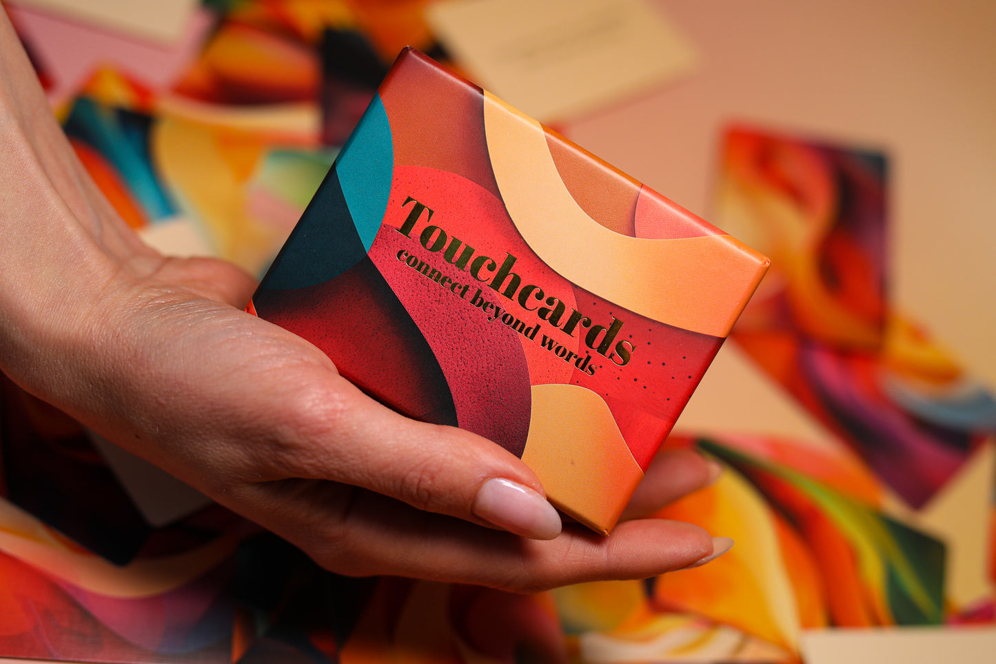 A hand holding a colorful box labeled 'Touchcards connect beyond words' against a warm, blurred background of matching abstract artwork.